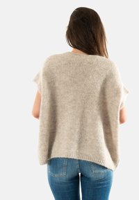 Suéter de punto color beige claro con mangas cortas, de corte holgado y acabado texturizado. Llevado sobre unos jeans de mezclilla claros, mostrando un estilo casual.