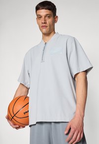 Light gray athletic shirt with short sleeves, a zippered collar, and a textured pattern. Holding an orange basketball.