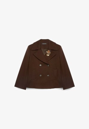 Bruine wollen dubbelgeknoopte jas met een grote reverskraag, twee voorzakken en een bloemrijke broche als accent aan de linkerkant van de borst.