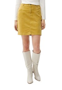 Senapsgul kordrock med fem fickor och knäppning framtill, ihop med knähöga vita stövlar. Slät textur genom hela plagget.