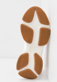 Valkoinen urheilukengän pohja, jossa on kuminen ulkopohja. Sisältää sahalaitakuvion ja sileän, pyöreän muodon.