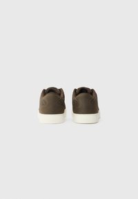 Zapatillas de ante marrón con textura trenzada en el talón, suela de goma blanca y cuellos acolchados. Diseño minimalista, vista trasera.