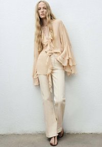 Pale peach flowing blouse with ruffled accents and a tie neckline, paired with cream wide-leg pants and brown slide sandals.