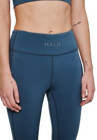 Hooggetailleerde teal yoga leggings met een zachte textuur, contrasterende naden en een klein "HALO" logo op de tailleband.