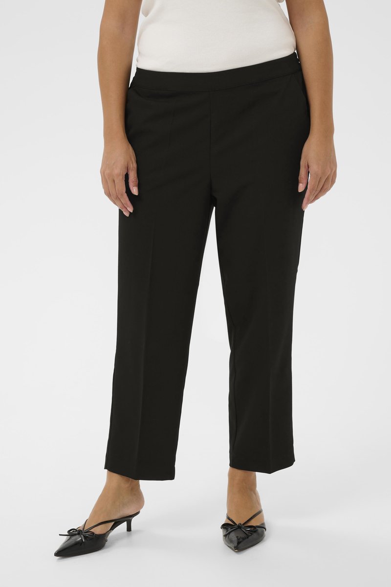 Pantalon noir sur mesure avec une coupe droite, une ceinture élastique et une texture lisse, associé à des chaussures noires à bouts pointus ornées d'un nœud.