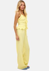 Conjunto amarillo de dos piezas que presenta un top corto acanalado con volantes y detalle de lazo, y pantalones de pierna ancha. La tela tiene un acabado suave y texturizado.