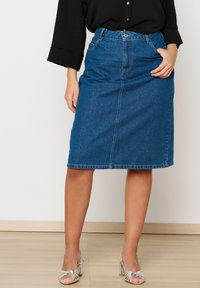 Denim svinčnik krilo v srednji modri barvi z sprednjim razporkom, petimi žepi, pasom z zankami in klasičnim ravnim krojem.