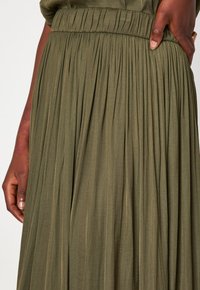 Gonna plissettata verde oliva con una texture morbida, caratterizzata da una vita elasticizzata arricciata e un tessuto fluente che si drappeggia elegantemente.