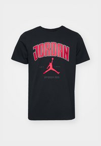 Černé bavlněné tričko s výrazným červeným textem "JORDAN" a siluetovým logem. Krátké rukávy, kulatý výstřih a grafické detaily na přední straně.