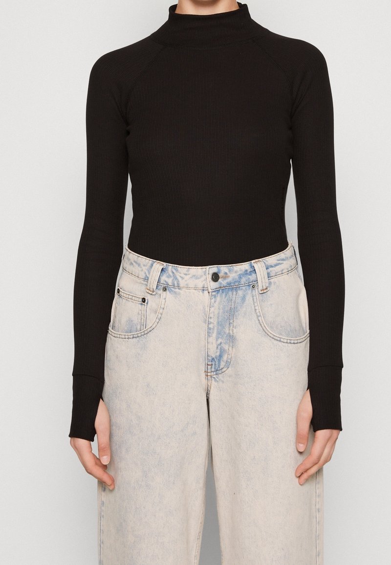 Un col roulé noir côtelé en tissu extensible, associé à un jean en denim taille haute bleu clair avec un design délavé et des poches.