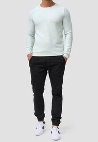 Heller Minzfarbener, langärmeliger, gerippter Pullover kombiniert mit schwarzen tapered Jogginghosen und weißen Sneakern mit schwarzen Akzenten. Minimalistisches Design und taillierte Passform.