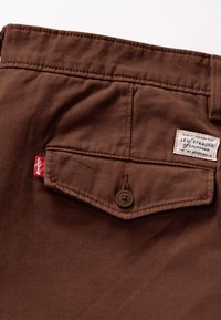 Catifea din bumbac maro cu o buzunar posterior, având un nasture maro și o etichetă Levi's cu text negru și accent roșu pe cusătura laterală.