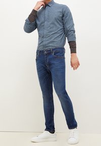 Randig blå skjorta med grå detaljer vid ärmarna, matchad med blå jeans och vita sneakers. Figurformad silhuett och avslappnad stil.