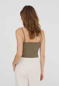 Top corto a coste verde oliva con spalline sottili, caratterizzato da un design aderente e tessuto testurizzato, abbinato a pantaloni a gamba larga di colore chiaro.