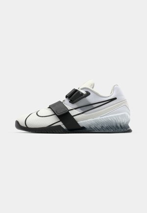 Sport shoe with a textured white upper, black strap, and gray translucent sole. Features black line accents along the sides.