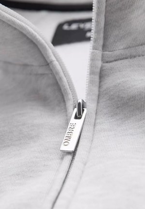 Grijze zip-up sweatshirt met een zilveren ritsdecoratie met 'OMBRE' gegraveerd. Zachte textuur en zichtbare stiksels.