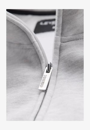 Grijze zip-up sweatshirt met een zilveren ritsdecoratie met 'OMBRE' gegraveerd. Zachte textuur en zichtbare stiksels.