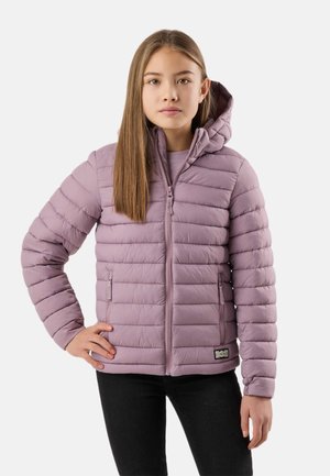 Ung pige står frontalt, iført en lys lilla dunjakke med hætte, den ene hånd på hoften, mod en ensfarvet lys baggrund.