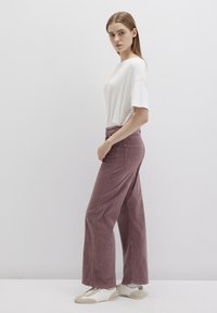Loose-fit, white short-sleeve shirt paired with high-waisted, ribbed, mauve wide-leg pants and white sneakers with textured accents.