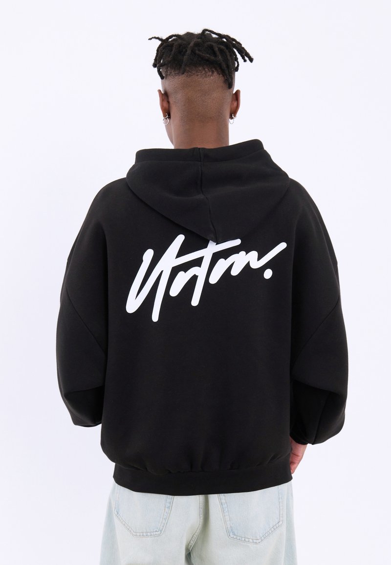 Felpa nera con vestibilità over size, caratterizzata da un logo script bianco sul retro. Realizzata in tessuto morbido, include un cappuccio con stringhe e orlo a coste.