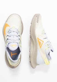 Chaussures de sport gris clair avec des accents jaunes et orange, dessus en mesh, semelle coussinée, et semelle extérieure texturée pour une adhérence optimale dans un design épuré.