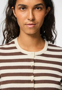Gestreepte cardigan in crèmekleurige en bruine brei, met een ronde hals en sluitingen met parelknoopjes aan de voorkant. Zachte textuur, aansluitend ontwerp.
