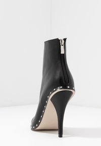 Mustat nahkasaappaat nilkkapituisilla korkeilla stiletto-koroilla, sivuvetoketjulla ja hopeisilla niiteillä kaarevan pohjan koristeluna.