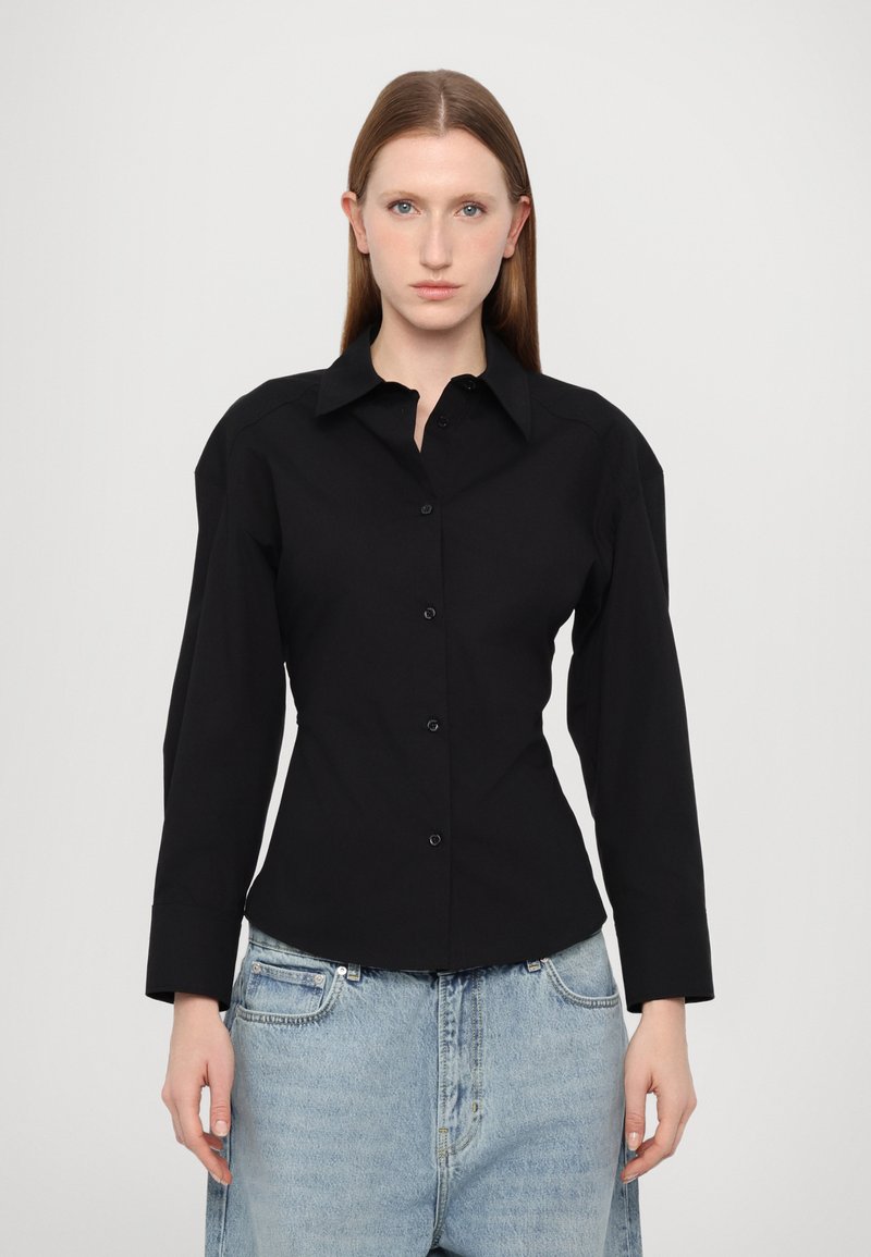 Svart knapp-up skjorte med strukturert passform, lange ermer og spiss krage, kombinert med løse jeans i lys vask.