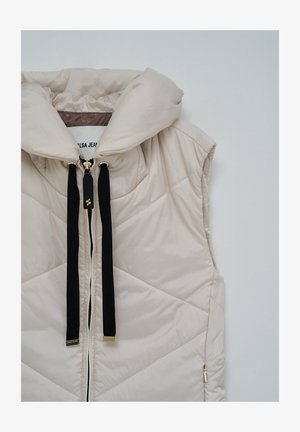 Beżowa pikowana kamizelka bez rękawów z wysokim kołnierzem, czarnymi sznurkami do ściągania i zamkiem błyskawicznym z przodu na jednolitym tle.