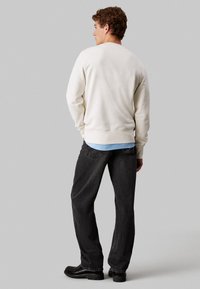 Sudadera de crema clara con cuello y puños acanalados, combinada con jeans gris oscuro y botas negras. Textura suave, ajuste relajado.