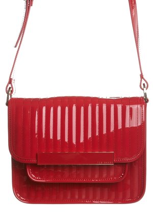 Sac bandoulière matelassé rouge brillant avec sangle réglable et fermeture à rabat rectangulaire, avec une gravure discrète de la marque sur une barre métallique.