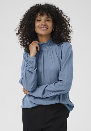 Light blue long-sleeve blouse with crinkled texture, high ruffled collar, and buttoned cuffs, paired with black trousers.