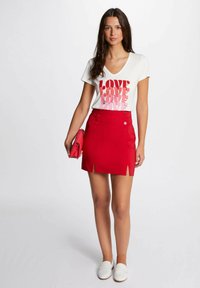 Mini gonna rossa con due fessure frontali, abbinata a una t-shirt bianca a scollo a V con la scritta "LOVE" in diverse sfumature di rosso, e accessoriata con una pochette rosa.