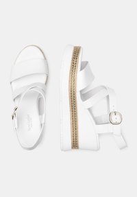 Hvide platform sandaler med krydset stropper, guldfarvet sål, justerbar ankelstrop og en glat mat finish.