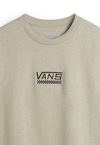 Lys beige t-shirt med et sort "VANS" logo og et ternet mønster nedenfor. Lavet af blødt stof med en standard rund hals.