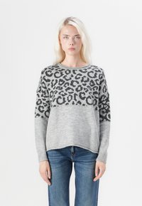 Pull en tricot gris avec un motif léopard sur la partie supérieure, manches longues et coupe décontractée, associé à un jean bleu.