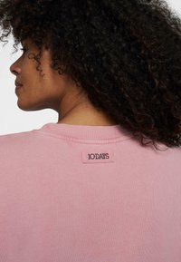 Lichtroze sweatshirt met een ronde hals, voorzien van geribbelde boorden en een merklabel op de achterkant van de nek. Zachte stof textuur.