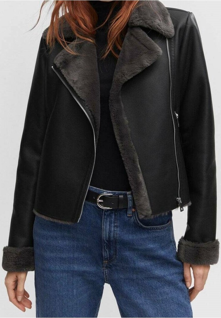 Veste en simili cuir noir avec un col et des poignets en fausse fourrure grise, dotée d'une fermeture éclair et d'un design court. Portée par-dessus un top noir.