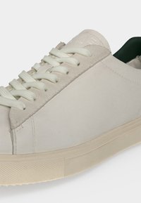 Άσπρο χαμηλό sneaker με λευκά κορδόνια που ταιριάζουν, σουέντ λεπτομέρειες κοντά στα περβάζια και υφασμένη λευκωπή λαστιχένια σόλα.