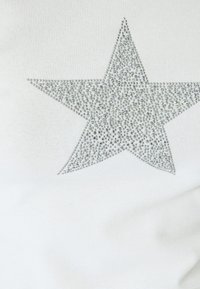 Hvidt stof med et stort sølv rhinestone stjernedesign, der har en tekstureret overflade og funklende accenter i hele stjernens form.