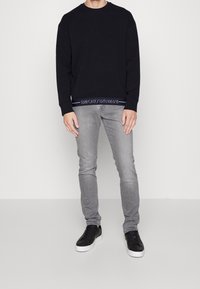 Svart sweatshirt med rund halsringning och logotyp nertill. Kombinerad med ljusgrå jeans och svarta sneakers med vit sula.