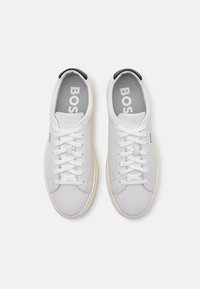 Vita lädersneakers med en slät yta, rund tå, platta snören, grå innesula med "BOSS"-logga och subtil märkning på sidan.