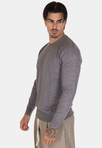 Maglione grigio a maniche lunghe in un morbido tessuto a maglia, con collo rotondo e polsini a coste, caratterizzato da un discreto etichetta del marchio all'orlo.
