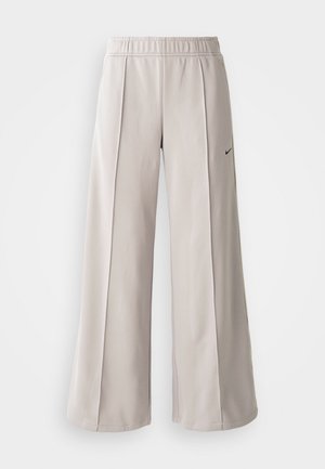 Pantalons larges gris clair en tissu lisse. Comprend une taille élastique et un logo Nike noir sur le côté gauche.