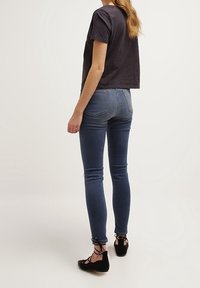 Maglietta nera cropped, jeans skinny blu con leggere abrasioni e scarpe nere basse con lacci alla caviglia, viste da dietro.