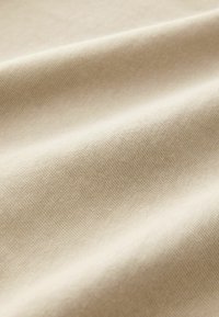 Tessuto beige con una texture liscia, caratterizzato da un sottile motivo di tessitura e delicate ondulazioni, che mettono in risalto le sue qualità flessibili e morbide.