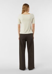 Krótki rękaw, bluzka w paski w jasnobeżowym kolorze z zielonymi paskami, połączona z szerokimi ciemnobrązowymi spodniami, widziana od tyłu.