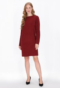 Vestido hasta la rodilla de manga larga en burdeos profundo, con un patrón de punto texturizado y un escote redondeado, combinado con tacones negros.