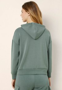Felpa con cappuccio in verde spento, con maniche lunghe, polsini a costine e una vestibilità comoda. Tessuto liscio e morbido con un design semplice.