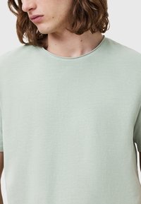 T-shirt verde menta a maniche corte in tessuto morbido e liscio. Presenta un collo a giro e una vestibilità rilassata, con una leggera texture sulla superficie.
